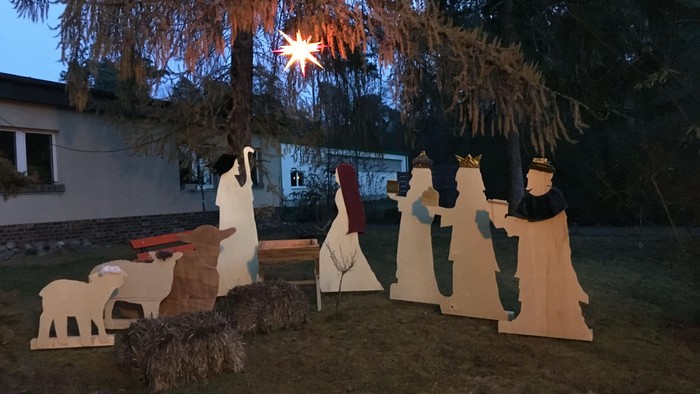 Im Garten steht eine Krippe mit Holzfiguren unter einem Baum