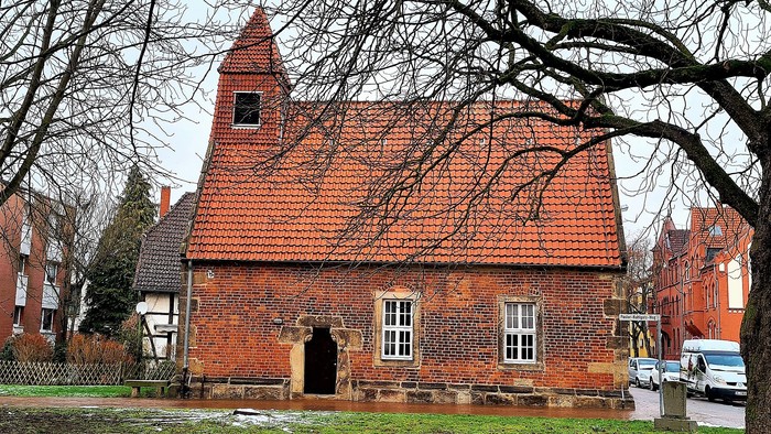 Ein altes Backsteingebäude mit rotem Dach und nackten Bäumen im Vordergrund