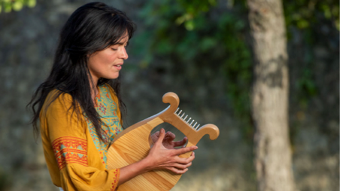 Une femme en robe jaune joue d'un instrument de musique en plein air.