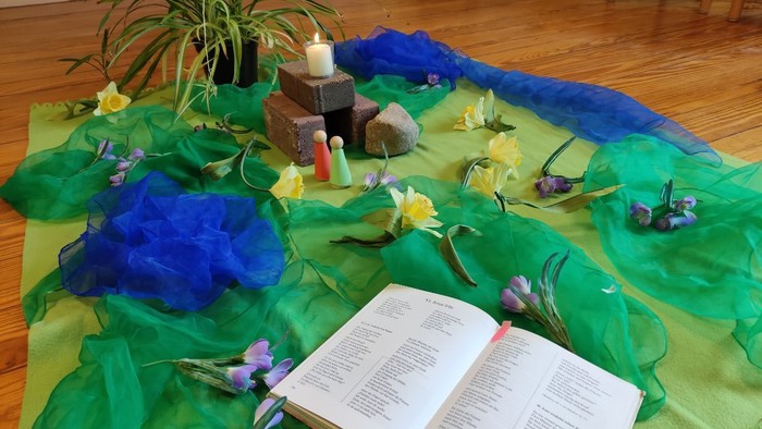 Ein Tisch mit grünen und blauen Tüchern, einer offenen Bibel, Kerzen und Blumen.