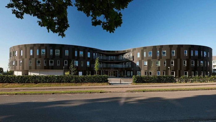 Stor, moderne bygning med mange vinduer og grønne arealer foran