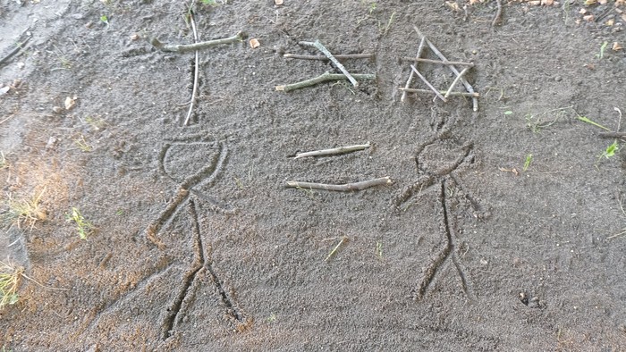 Holzstöcke im Dreck angeordnet wie Menschen und Symbole