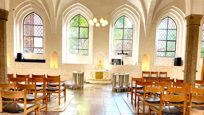 Indre del af kirke med træstole og alter.