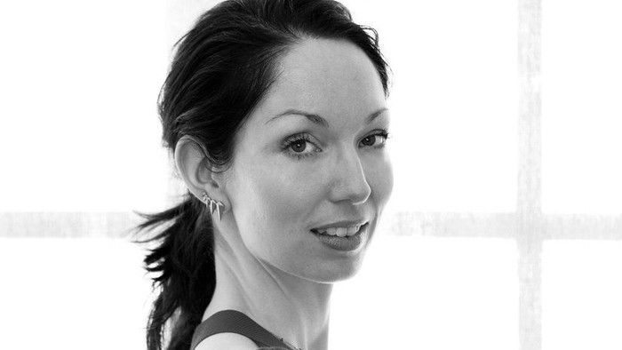 Kvinde med korslagte arme, smilende, stående nær vindue.