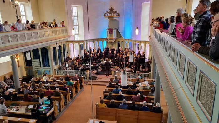 Großer Saal mit vielen Menschen, einige sitzen, andere stehen und reden.