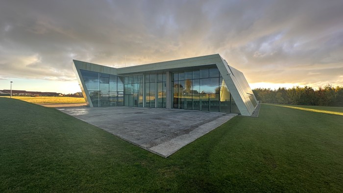 Moderne bygning med glasfacader og skråt tag i grønne omgivelser ved solnedgang