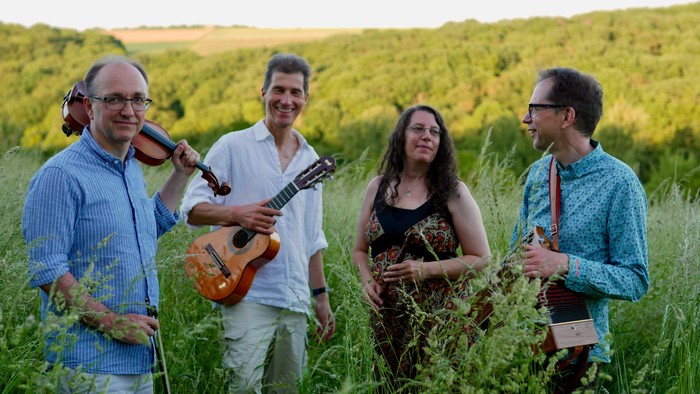 Ein Quartett von Musiker:innen, das verschiedene Instrumente auf einer üppigen, grünen Wiese im Freien spielt.
