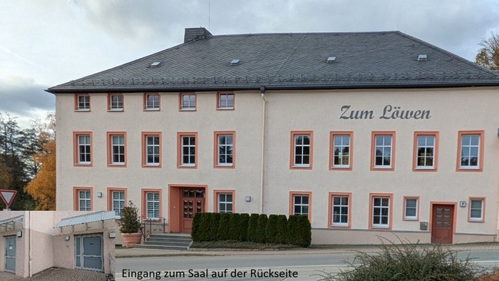 Ein großes zweigeschossiges Gebäude mit dem Schild *„Zum Löwen“*, umgeben von Grünflächen und einem bewölkten Himmel.