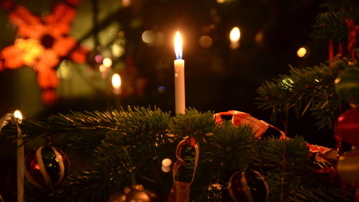 En lysende stearinlys på en grønne krans med røde bænder i en mørk og festligt belyset rum