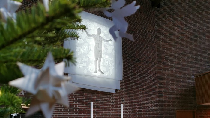 En indendørs julestjerne foran et vinduesglas med motiv.