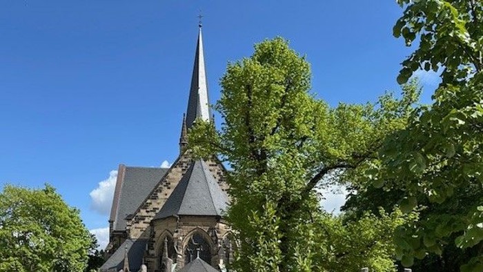 Ein hölzernes Kirchlein mit spitzem Turm in einem grünen Garten