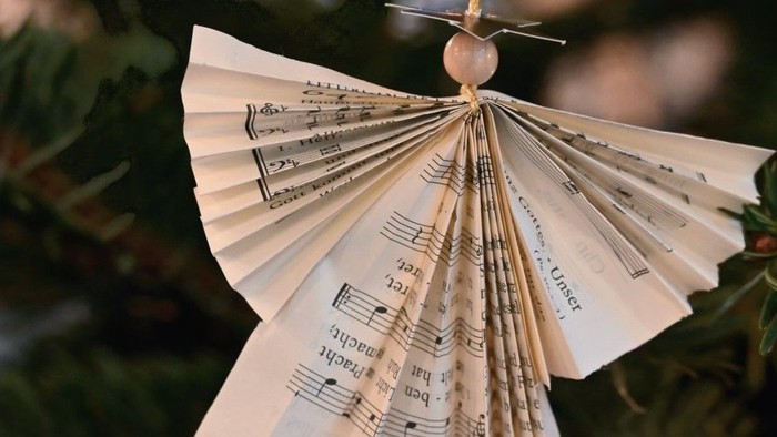 Ein gefalteter Papierengel mit Notenblättern hängt an einem Weihnachtsbaum.