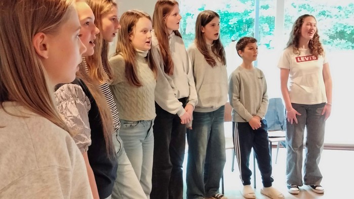 En gruppe unge piger står i en hal og synger.