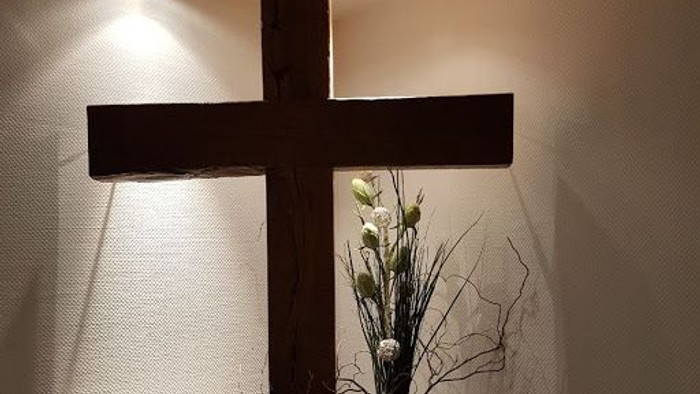 Ein hölzernes Kreuz an der Wand mit einer Vase voller Blumen darunter