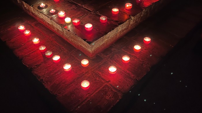 Mehrere rote Kerzen in Holzkisten auf einem Holzboden.