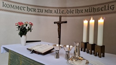 Altar mit Kreuz, Kerzen, Blumen und Buch, deutsche Inschrift