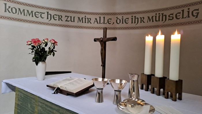 Altar mit Kreuz, Kerzen, Blumen und Buch, deutsche Inschrift