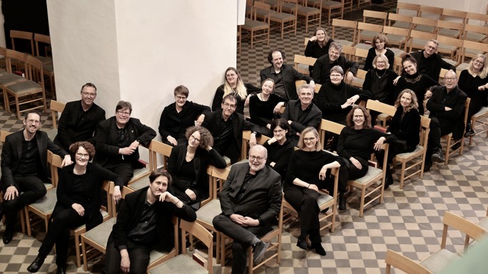 Gruppe von Personen in schwarzer Kleidung, die in Reihen von Stühlen sitzen