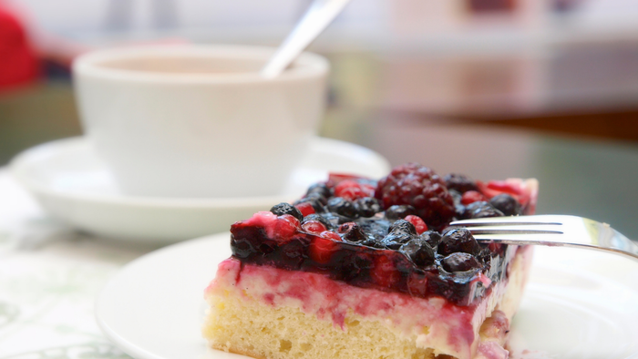 Ein Stück Kuchen mit Beeren und ein Kaffee in einer Tasse auf einem Tisch