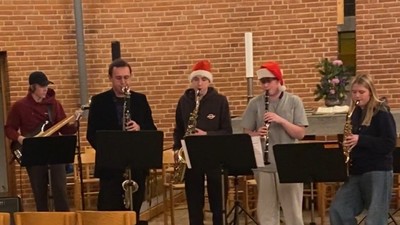 Musikere optræder i festligt tøj foran en murstensbaggrund.