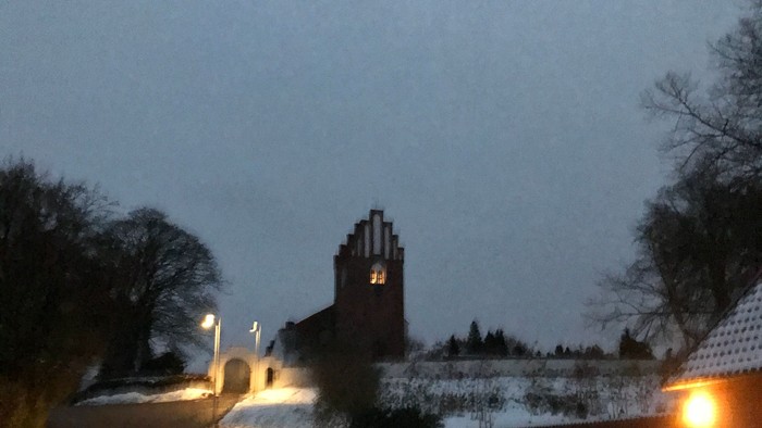 En mørk nattehavn med en belyset bro og en kirke i baggrunden