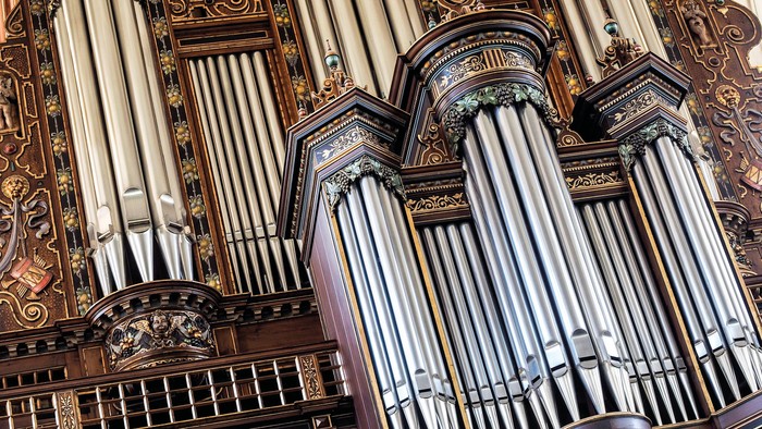 Komplekst pibeorgel med udsmykket træbeklædning og talrige sølvfarvede piber arrangeret i elegante rækker.