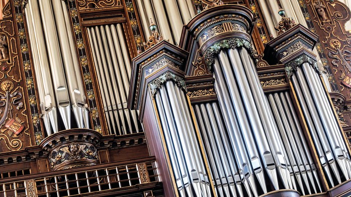 Komplekst pibeorgel med udsmykket træbeklædning og talrige sølvfarvede piber arrangeret i elegante rækker.