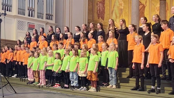 Eine Gruppe von Kindern und Erwachsenen posiert in einer Kirche, viele Kinder tragen orangefarbene Hemden.