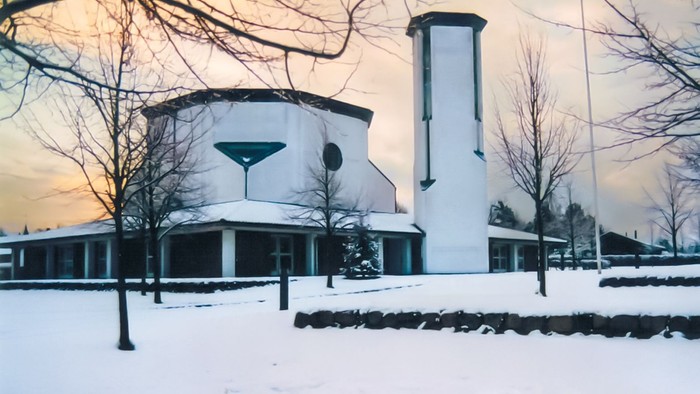 Bygning dækket af sne med høj skorsten og bare træer.