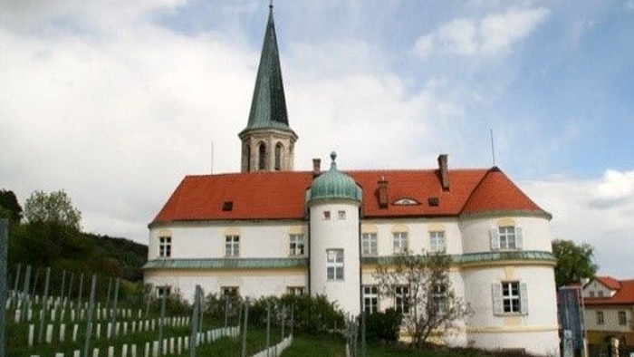 Weißes Gebäude mit rotem Dach und hoher Spitze, umgeben von einem Friedhof