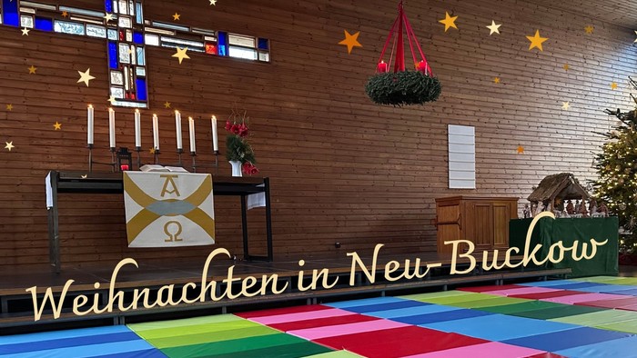 Nahaufnahme vom Kirchsaal Neu-Buckow mit dem Buntglas-Kreuz. Vor den Stufen liegen großflächig bunte Turnmatten für Kinder ausgebreitet. 