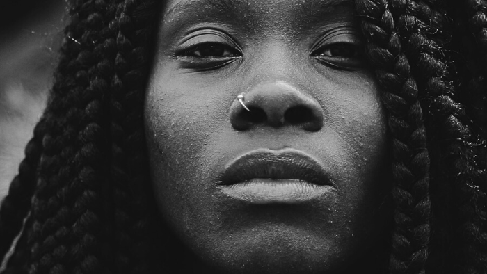 Ein auffälliges Schwarz-Weiß-Porträt einer Person mit langen geflochtenen Haaren und einem nachdenklichen Gesichtsausdruck.