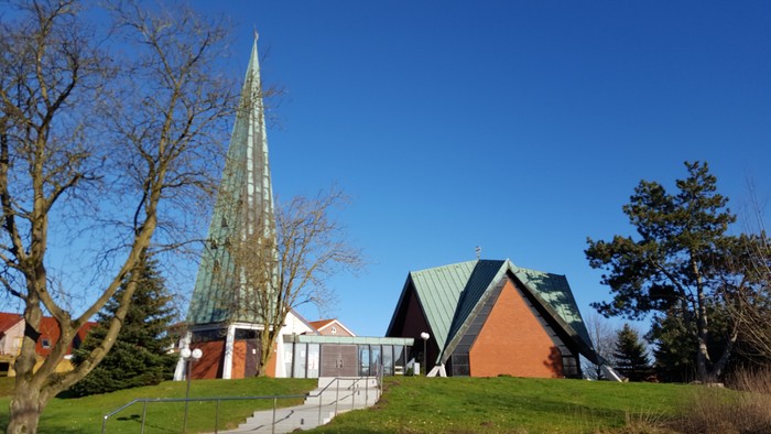 Kirche mit hohem Turm und grünem Dach auf grasigem Hügel