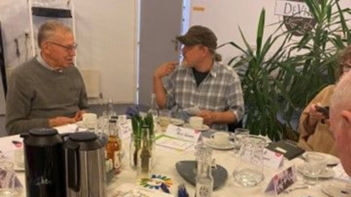 En gruppe mennesker sidder ved et bord med kage og teetøj.