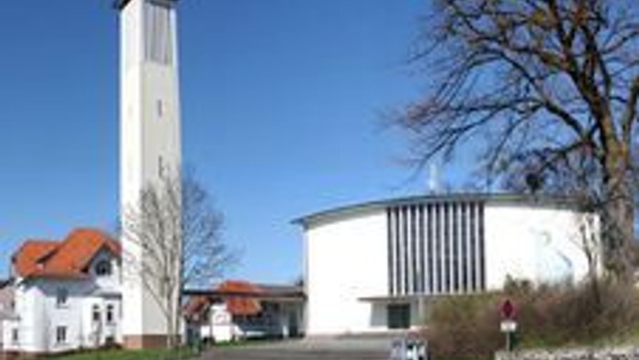 Moderne Kirche mit hohem Glockenturm und runder Kapelle in einer ruhigen, landschaftlich gestalteten Umgebung.