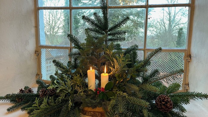 En lille juletræ på vinduesbank med to lysende lygter og granegren.