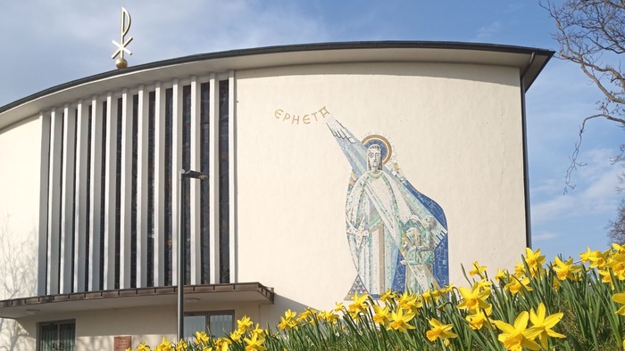 Moderne Kirche mit Wandgemälde eines Heiligen, umgeben von leuchtend gelben Osterglocken im Frühling.