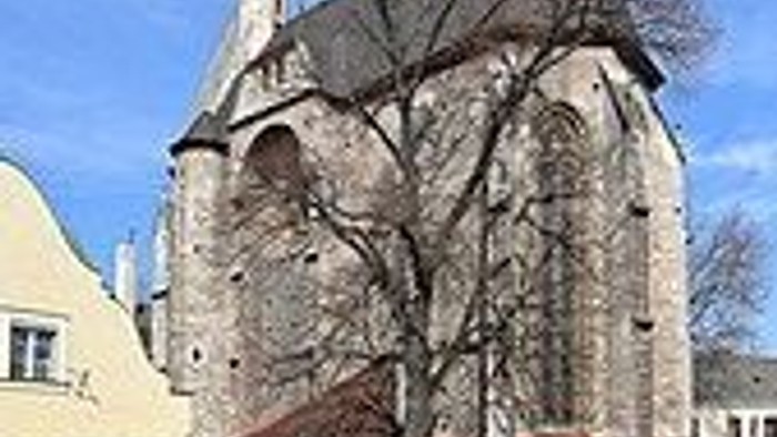 Historische Steinkirche mit hohem Turm und angrenzenden Wohngebäuden unter klarem blauem Himmel.