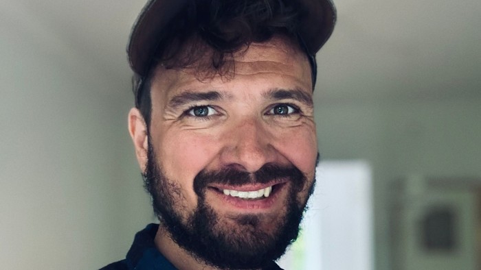 En smilende mand med barber og baseballmåtte.