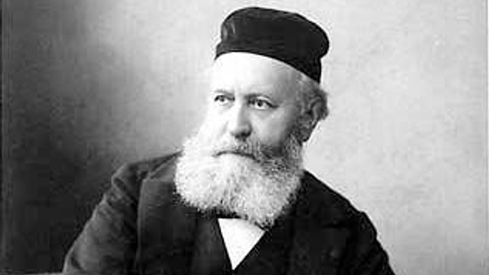 Ein bärtiger Mann in traditioneller Kleidung hält ein Buch.