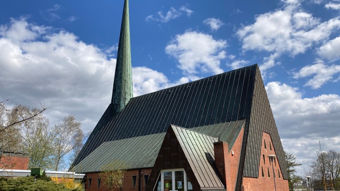 Kirchengebäude mit hohem Turm und grünem Dach unter blauem Himmel