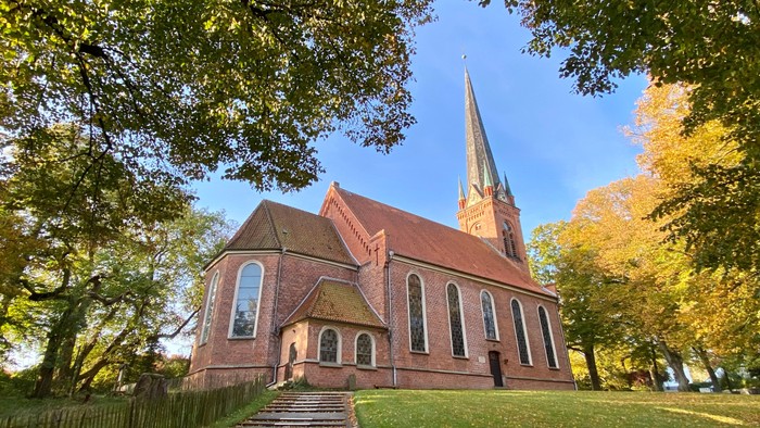 Kirchengelände mit hohem Turm, umgeben von Bäumen im Herbstlaub