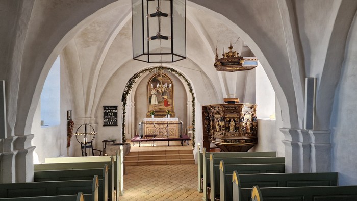 Indre del af kirke med bænke, lysstake og alter.