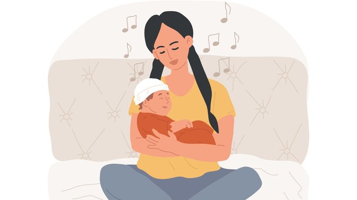 Eine Frau hält ein Baby im Arm und sitzt auf einem Bett.