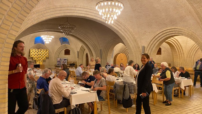 En gruppe af mennesker sidder og spiser i en underjordisk restaurant med buede vægge og hængende lygter.