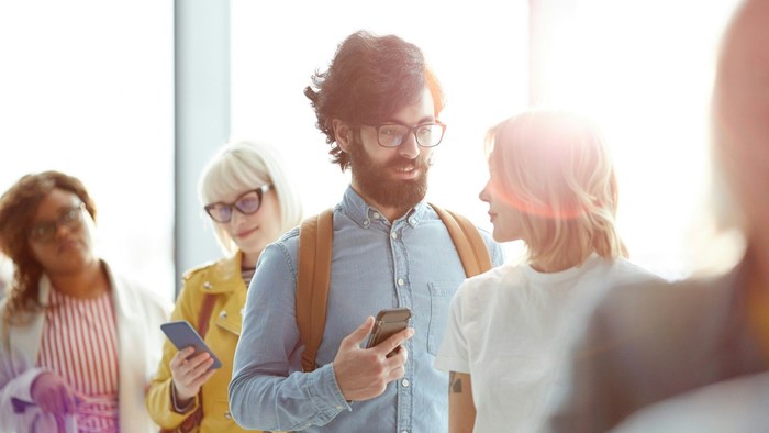 Drei Frauen und ein Mann stehen in einer Schlange reden miteinander und kommunizieren zugleich mit ihren Handys.