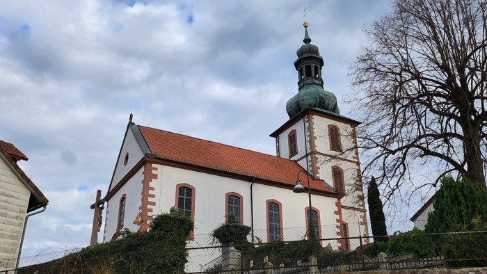 Weiße Kirche mit rotem Dach und grünem Turm auf Hügel.