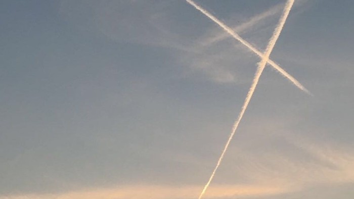 Ein Kirchturm vor einem Himmel mit Sonnenuntergang und Kondensstreifen