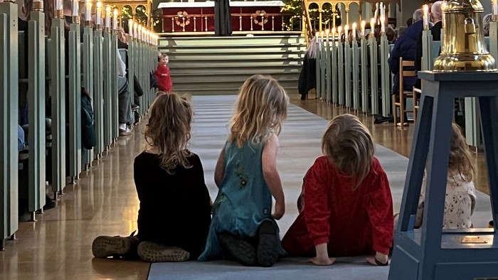 Tre børn sidder i en kirke.
