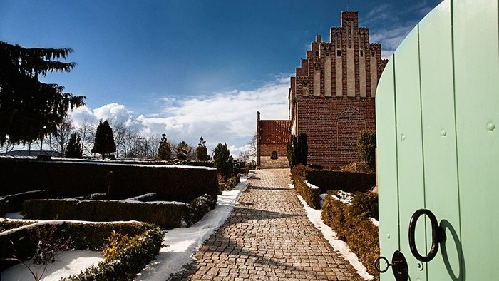 En stenvej leder op til en middelalderlig borg med tårn, omgivet af sne og træer